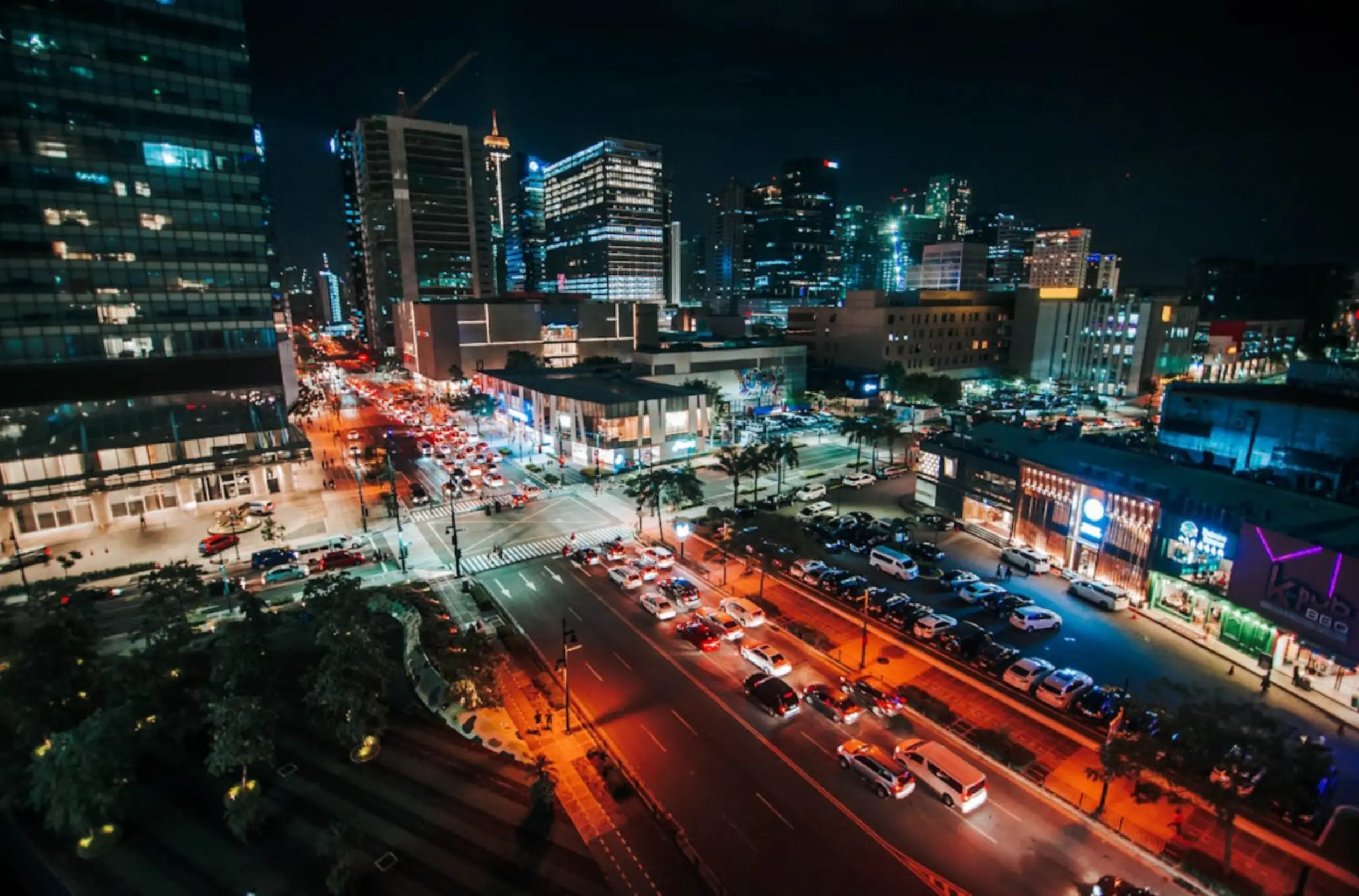 A dynamic night time cityscape of Makati, Philippines, showing brightly lit streets, buildings, and heavy traffic, capturing the city's lively atmosphere after dark.